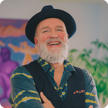 Underviser hos Academy Copenhagen Morten står foran maleri og plante og smiler